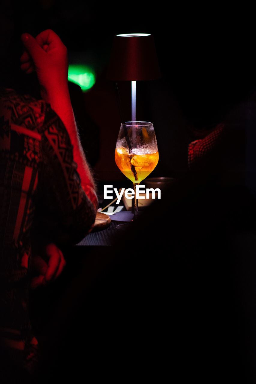 darkness, alcohol, glass, drink, refreshment, red, wine glass, wine, night, food and drink, indoors, light, drinking glass, one person, lighting equipment, lighting, dark, household equipment, illuminated, adult, nightlife, drinking, lifestyles, leisure activity, table