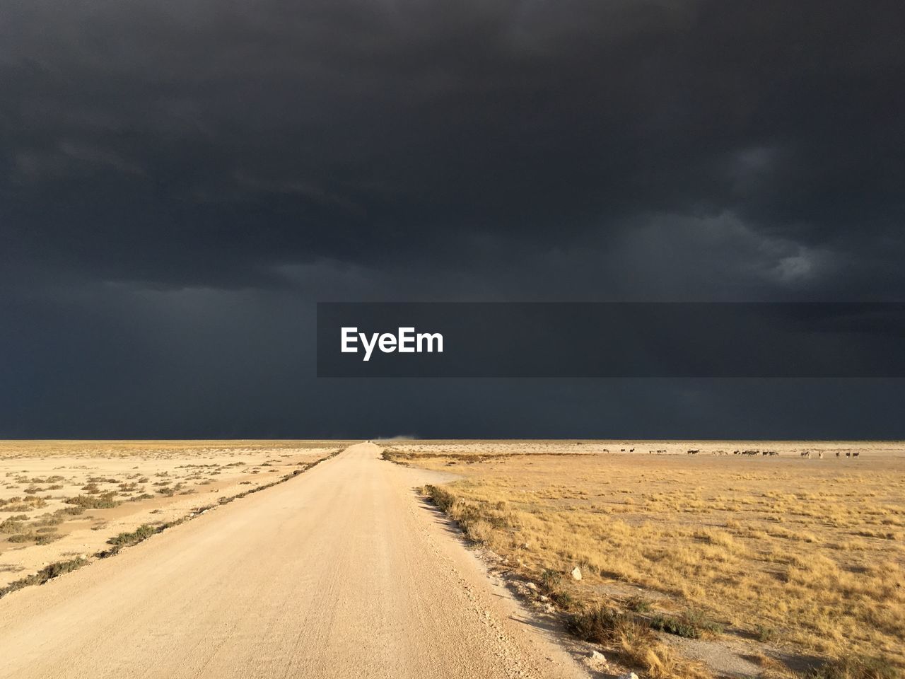 Road passing through land against storm clouds