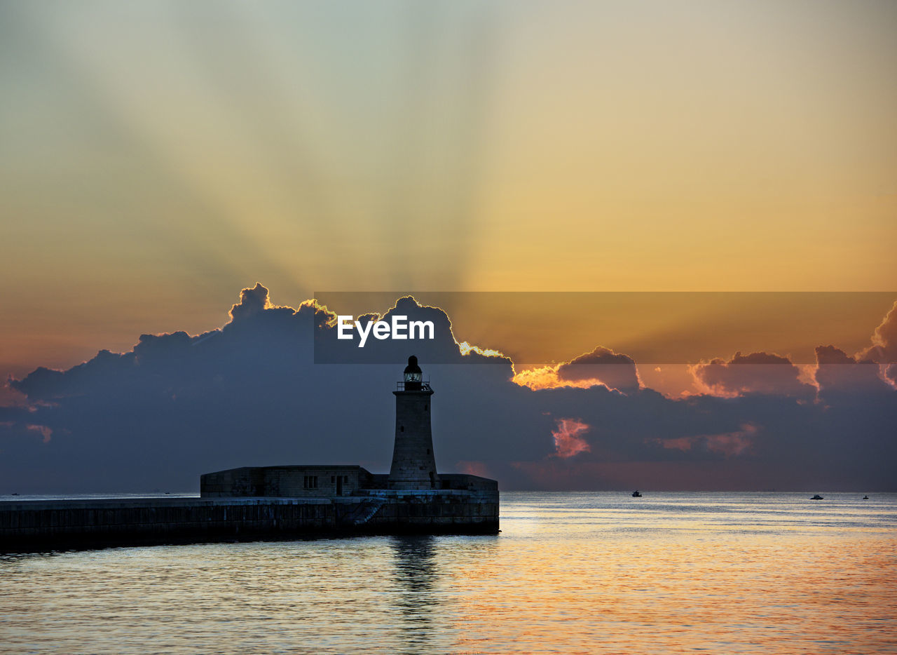 SILHOUETTE OF LIGHTHOUSE AT SEASIDE DURING SUNSET