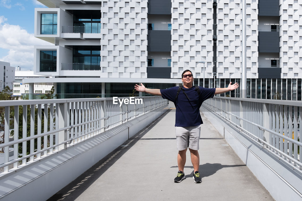 Full length portrait of smiling man standing on bridge in city