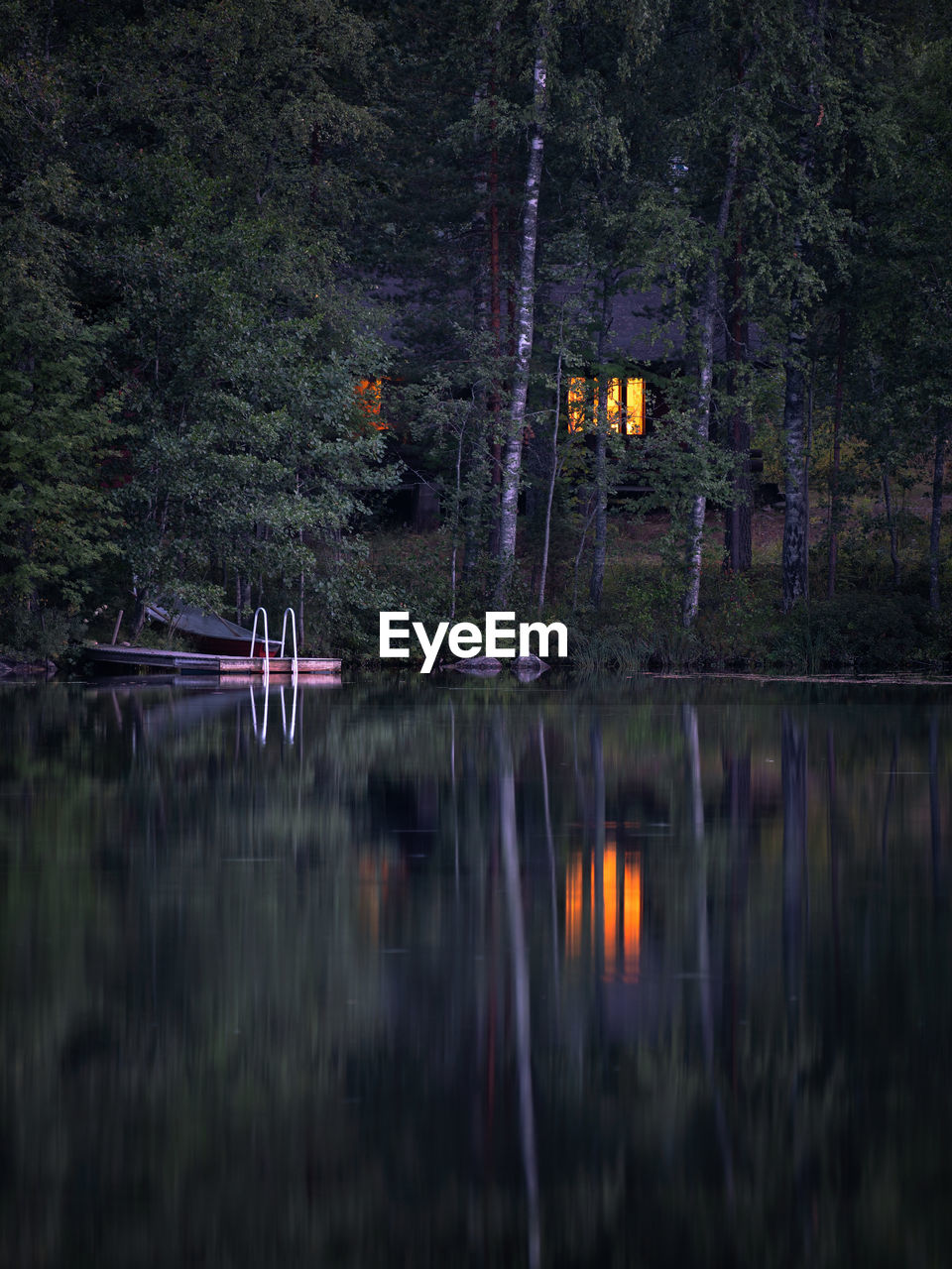 Reflection of trees and keinoja cottage in lake at summer night
