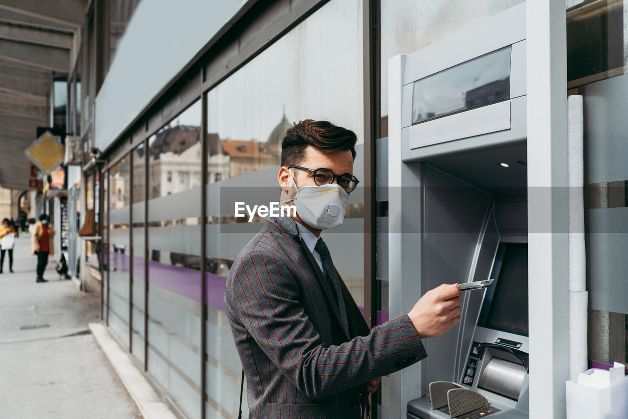 Business man with protective face mask using street atm machine.