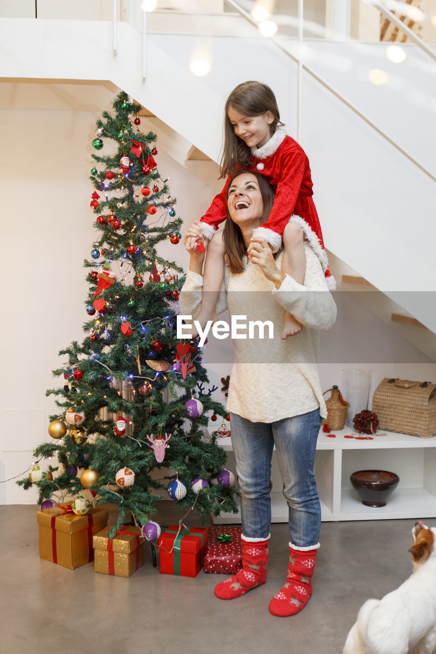 Happy mother carrying daughter on shoulders while standing by christmas tree