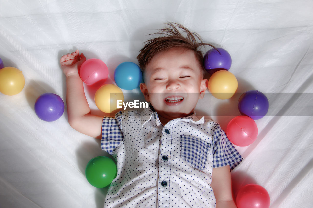 High angle view of boy playing with balloons while lying on bed at home