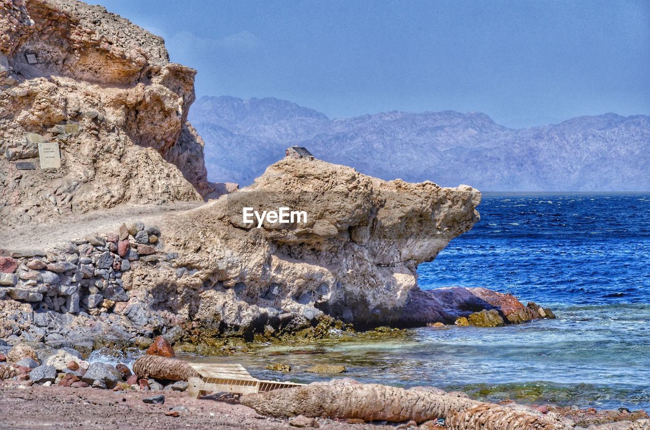 Rocks on shore by sea against sky