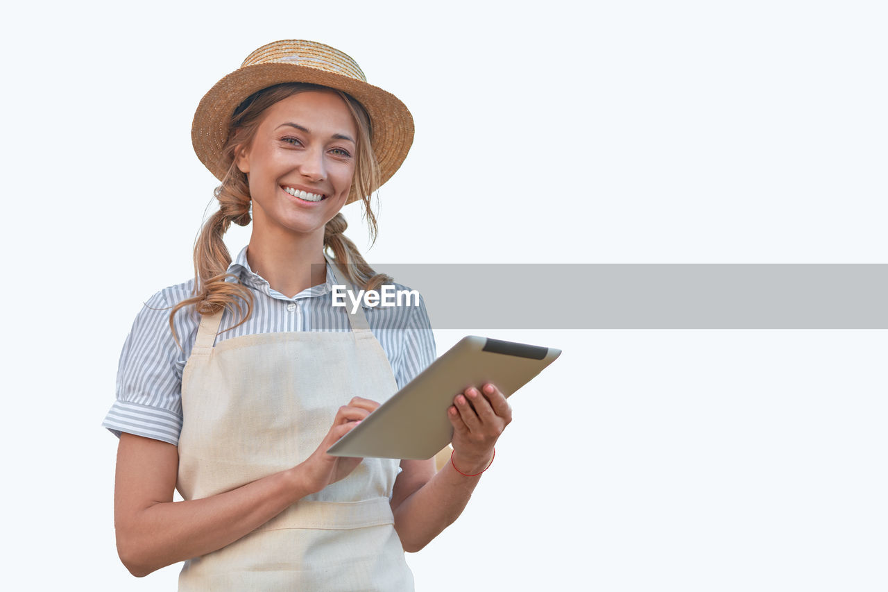 PORTRAIT OF SMILING YOUNG WOMAN STANDING AGAINST WHITE BACKGROUND