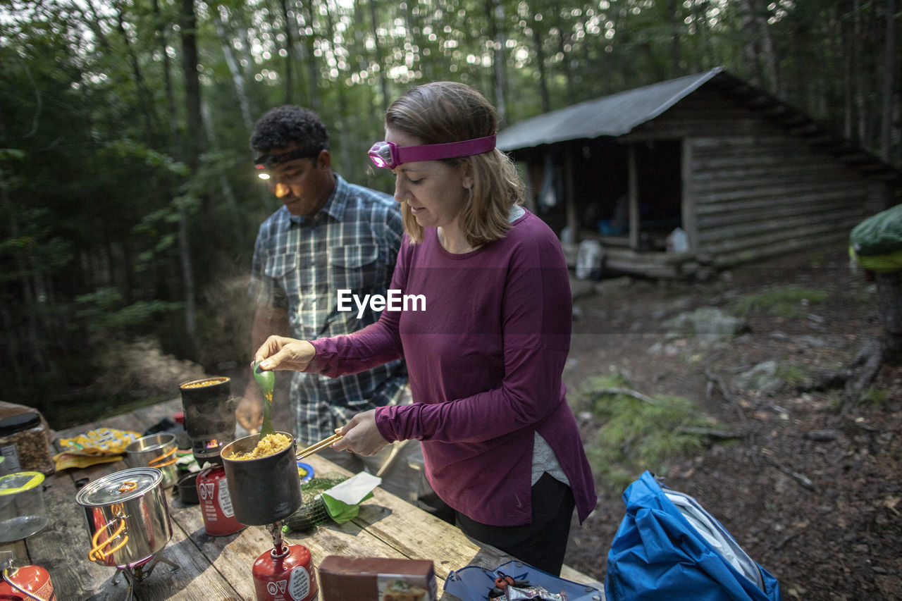 Couple with headlamps cook in front of appalachian trail shelter maine
