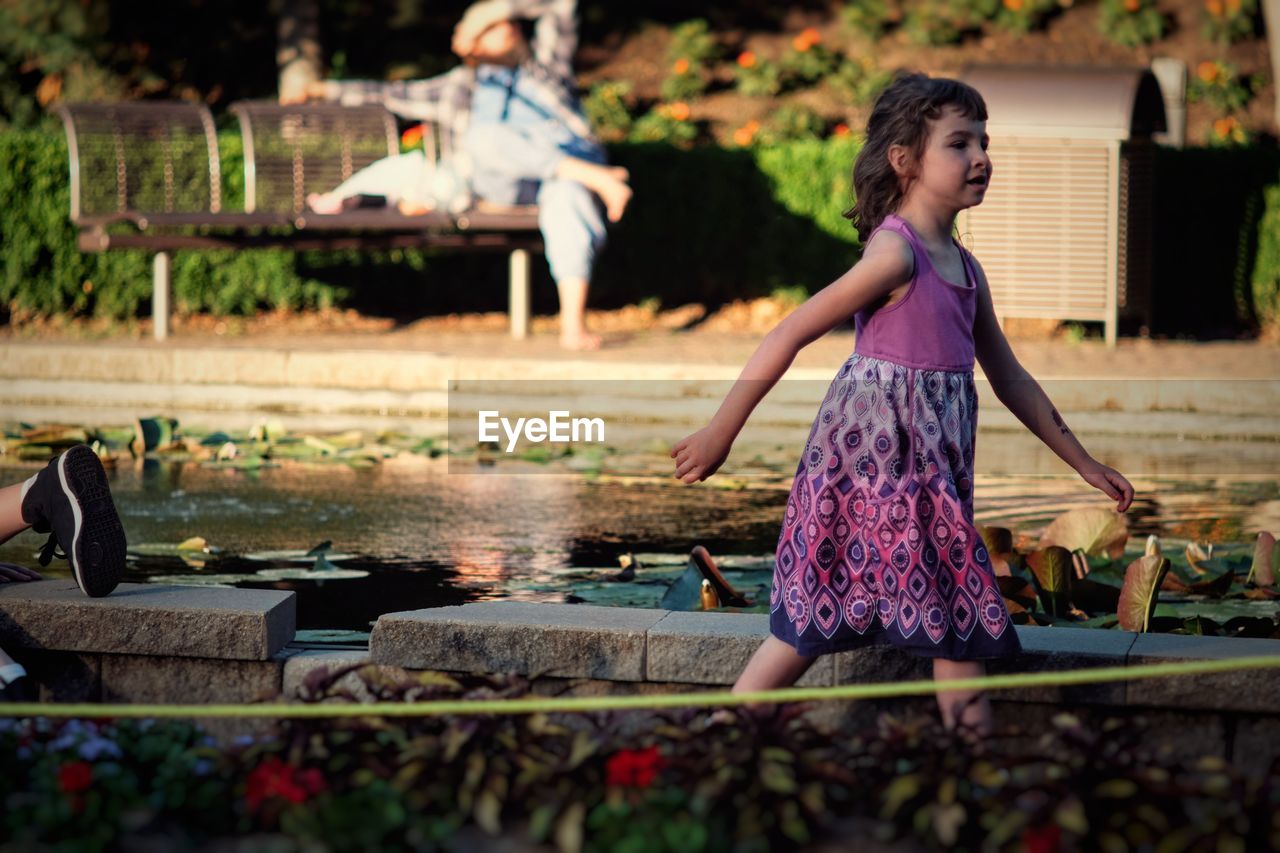 Side view of cute girl looking away while walking by pond in park