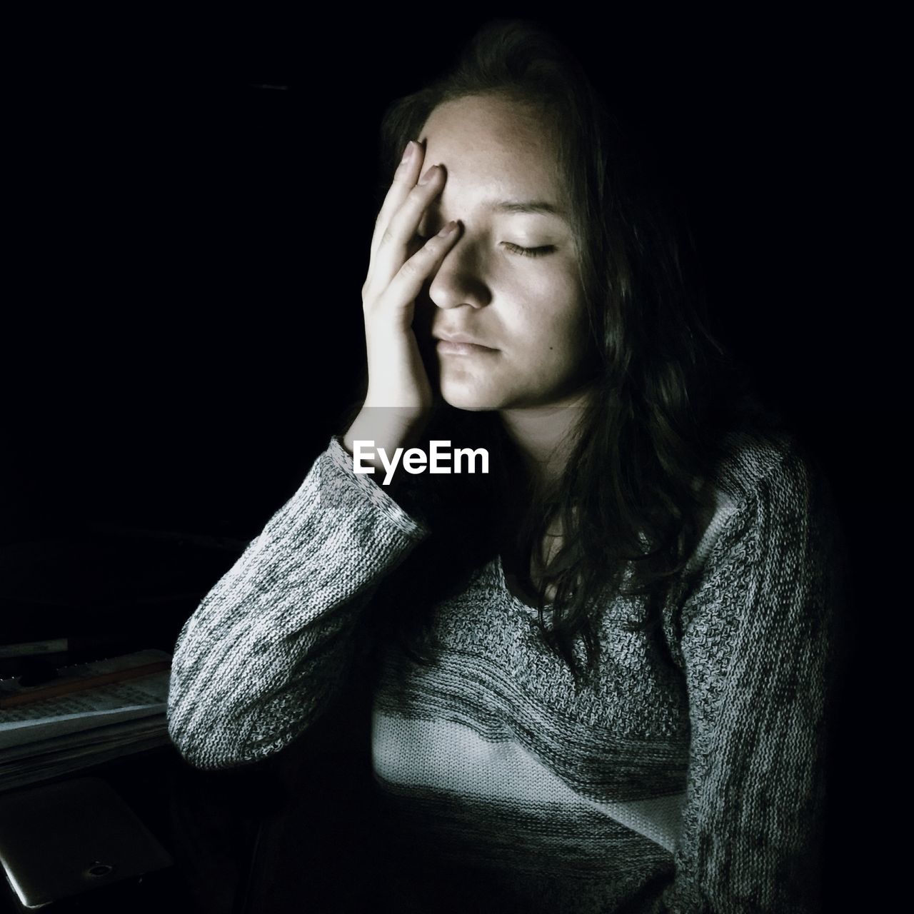 Sad young woman sitting against black background