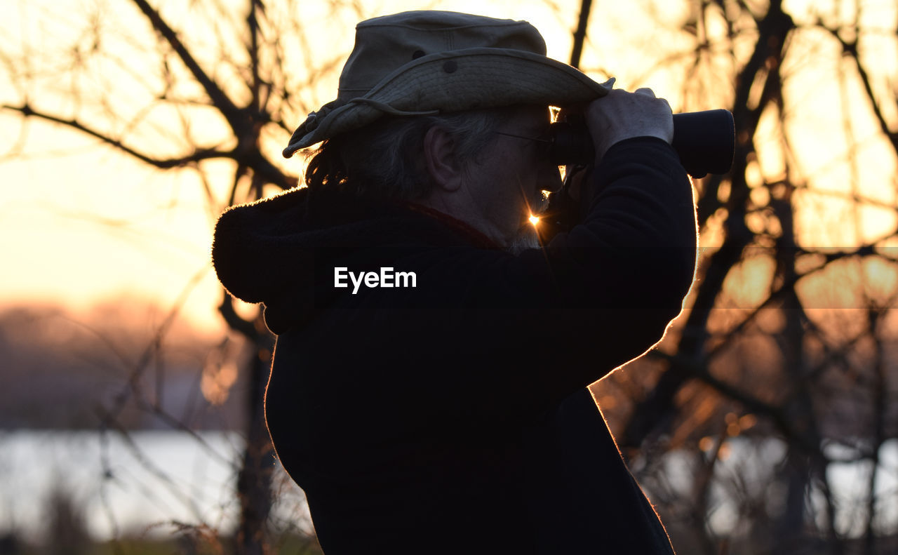 Rear view of silhouette man photographing against sunset sky