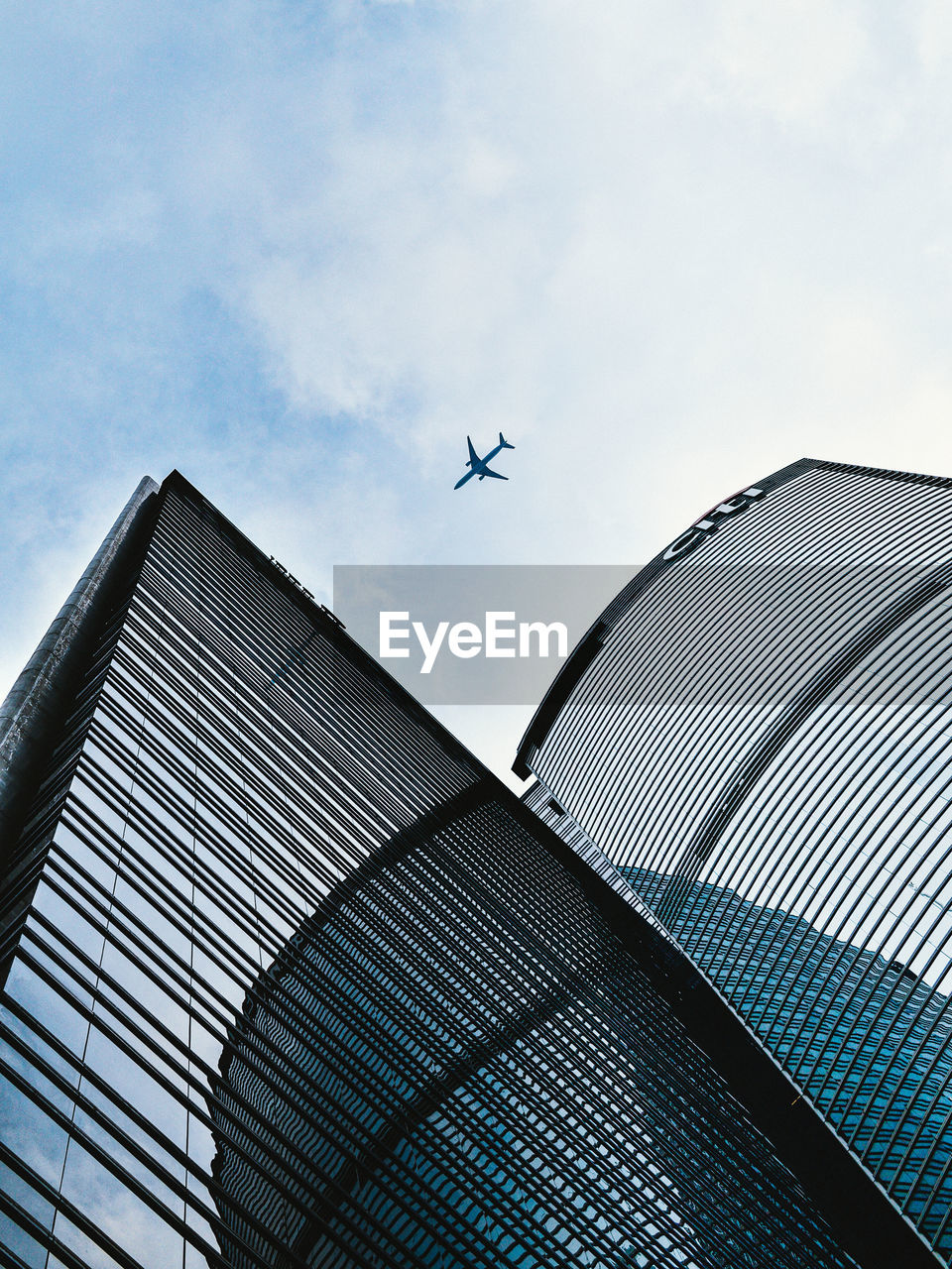 LOW ANGLE VIEW OF MODERN BUILDING AGAINST AIRPLANE