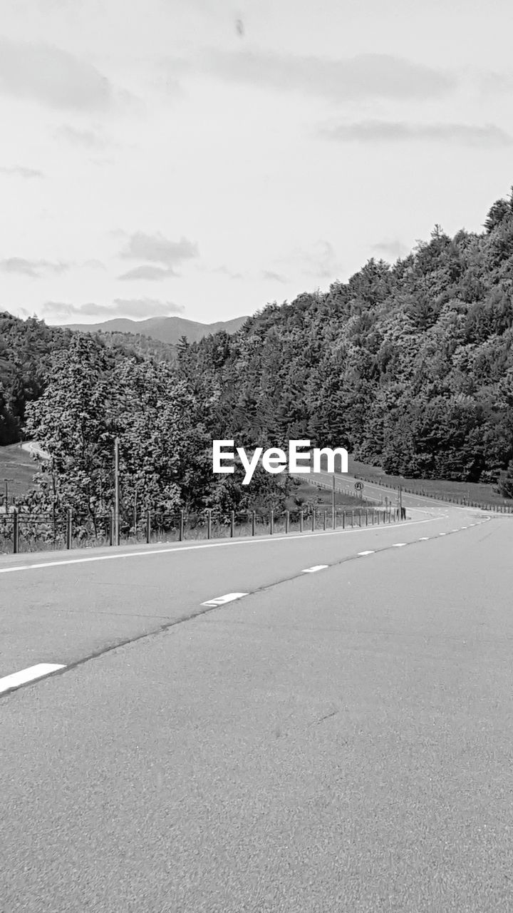 Road by trees against sky