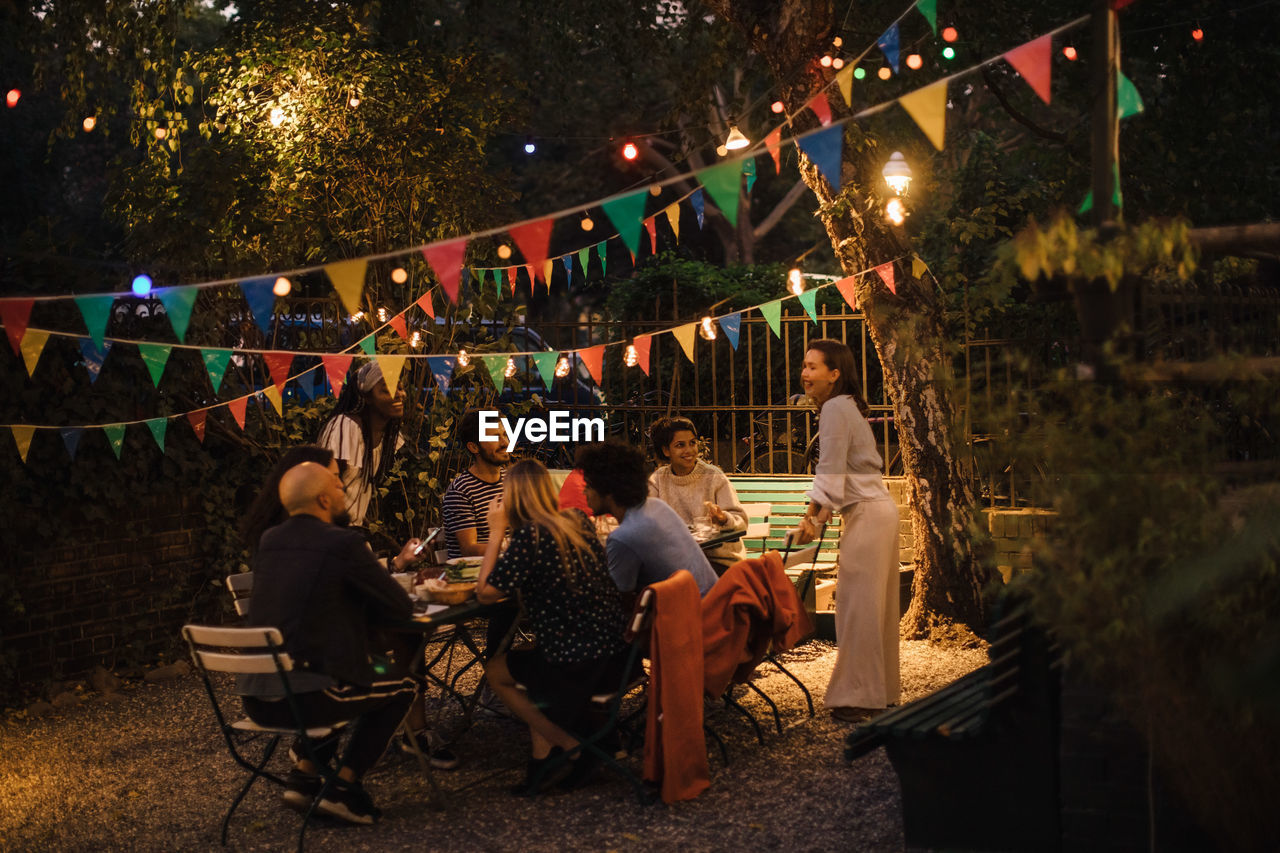 Multi-ethnic male and female friends enjoying dinner party in illuminated backyard