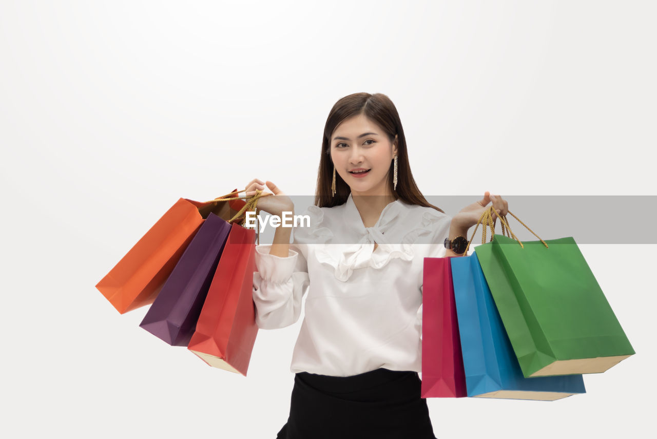 Portrait of smiling woman holding shopping bags while standing against white background