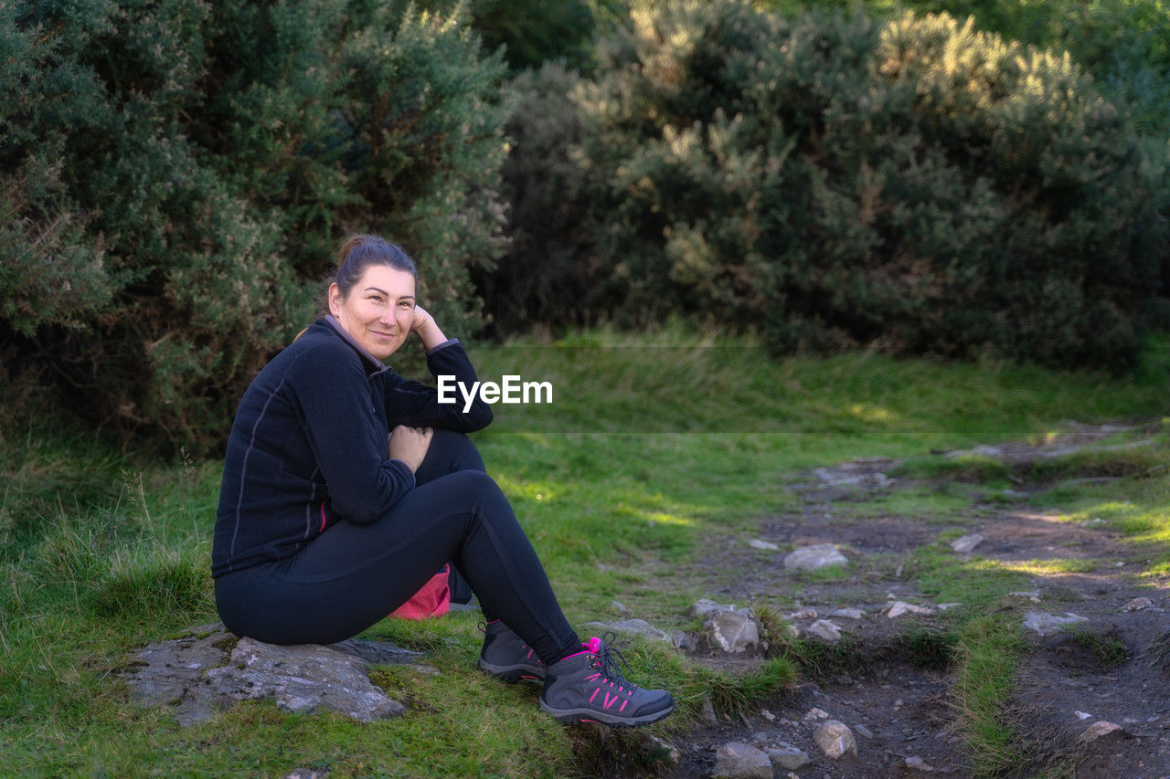 Adult woman sitting on a rock in the forest, hiking in glendalough, wicklow mountains, ireland