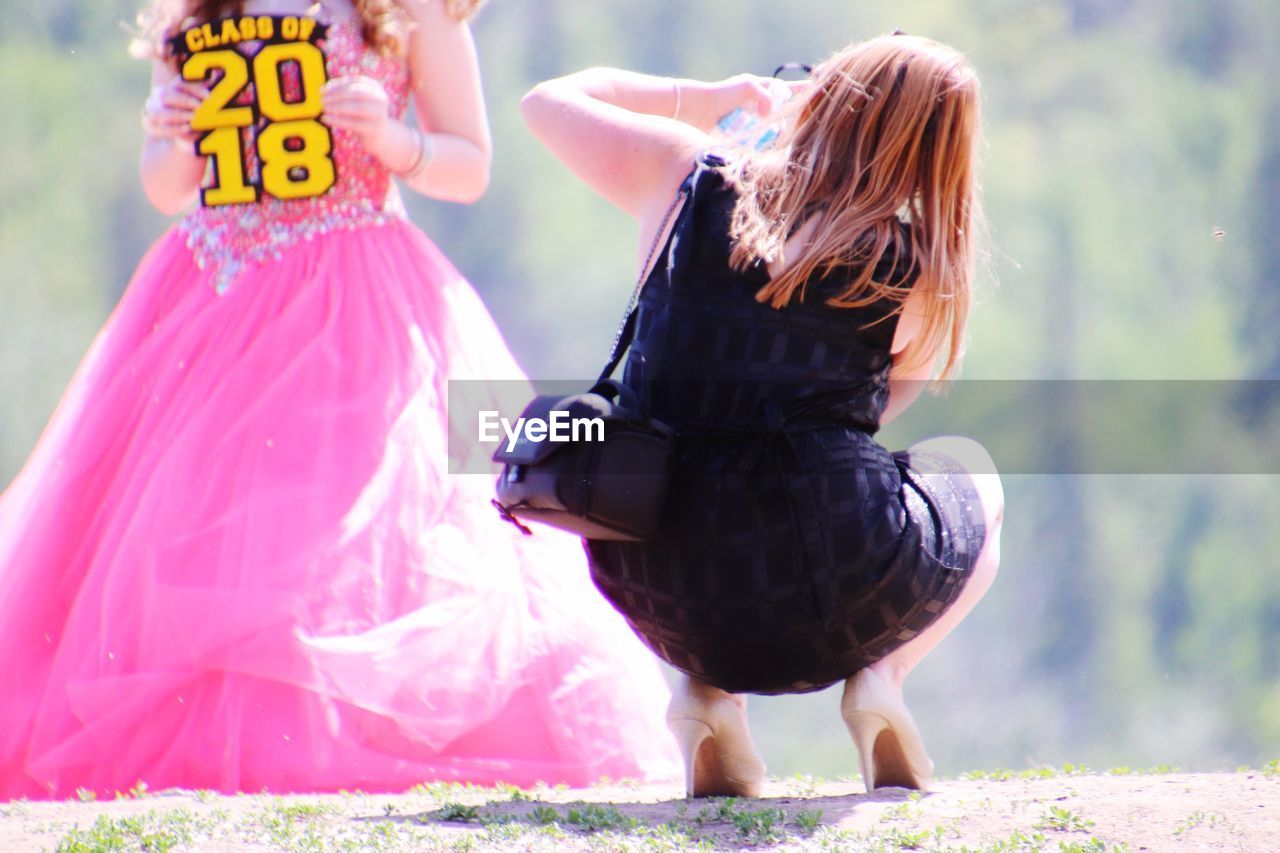 REAR VIEW OF WOMAN WITH ARMS RAISED STANDING AGAINST PINK BACKGROUND