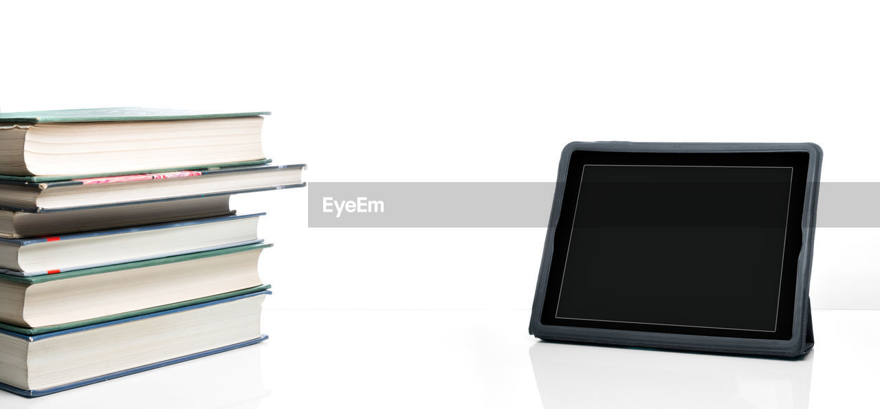 Close-up of books stacked by digital tablet on table against white background