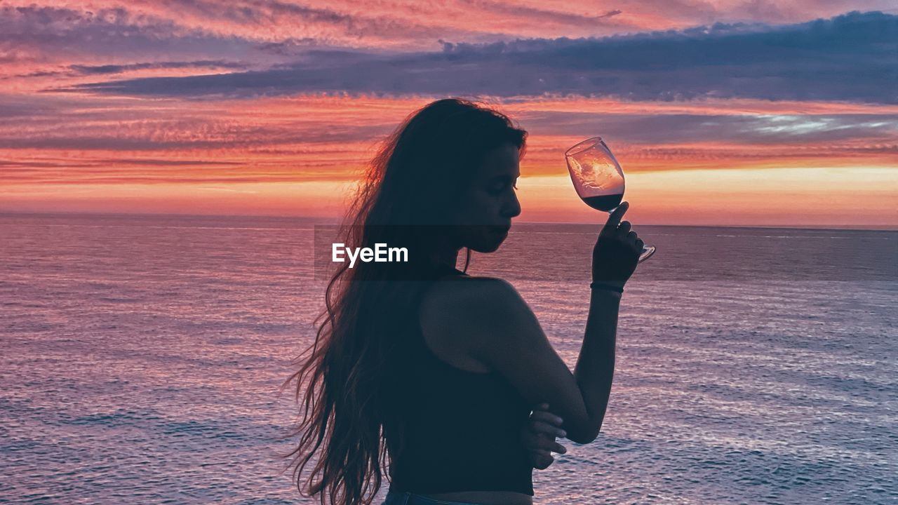 WOMAN DRINKING WATER AT BEACH AGAINST SKY