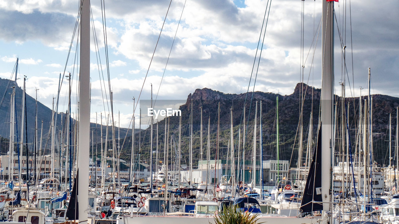 Sailboats in harbor against cloudy sky