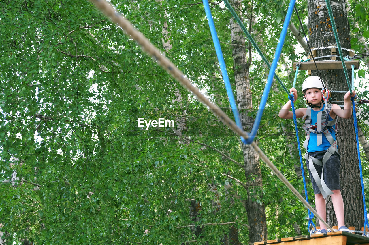 Child boy having summer fun at adventure park on the zip line. balance beam and rope bridges