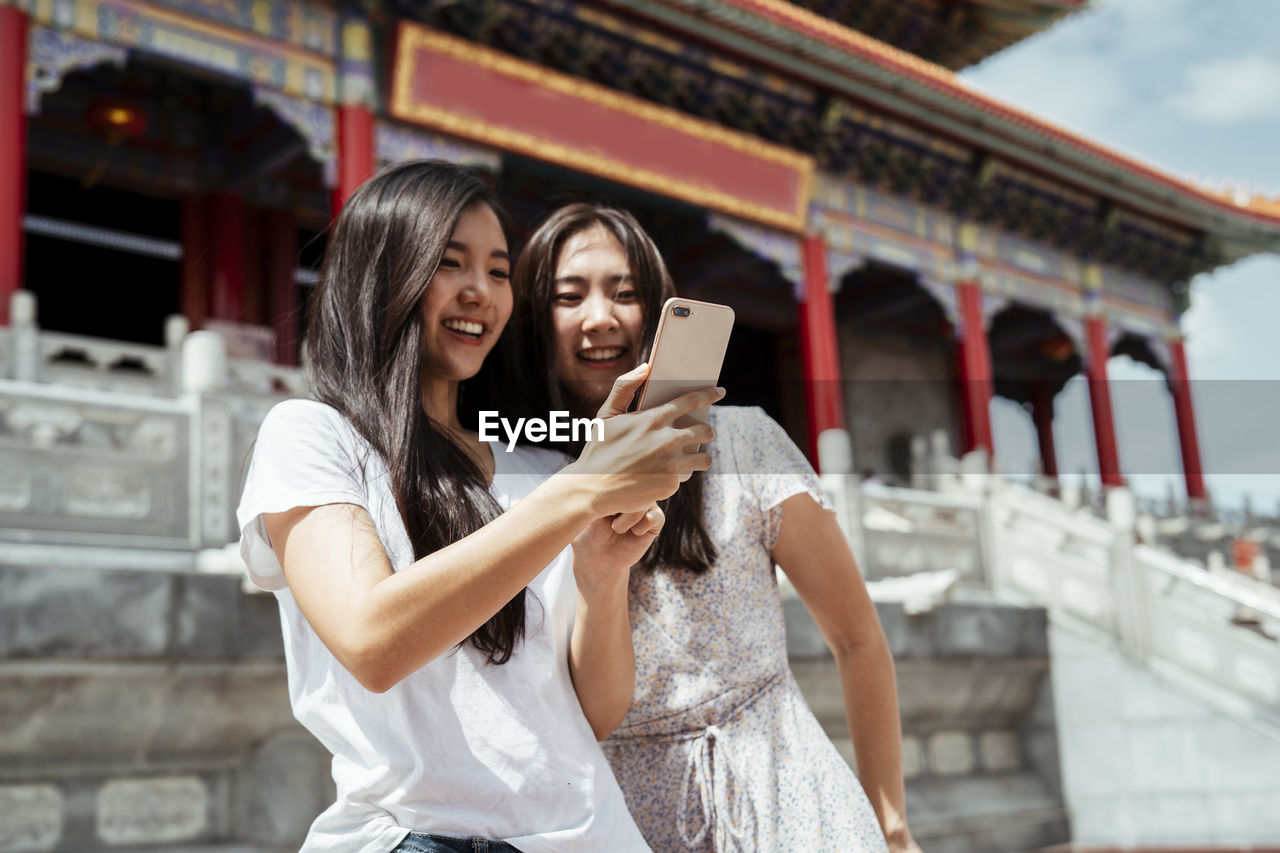 Smiling women vlogging while standing against temple
