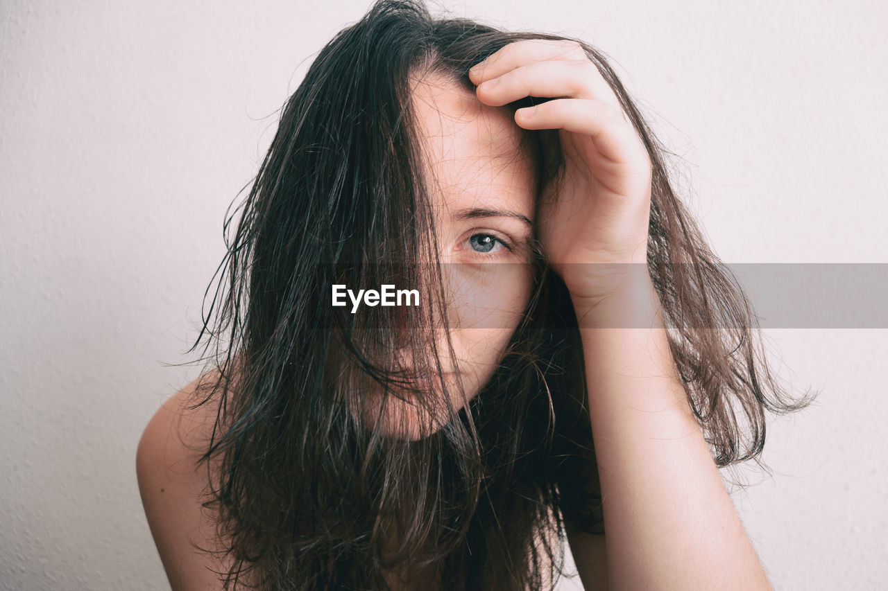 Portrait of young woman with messy hair against wall