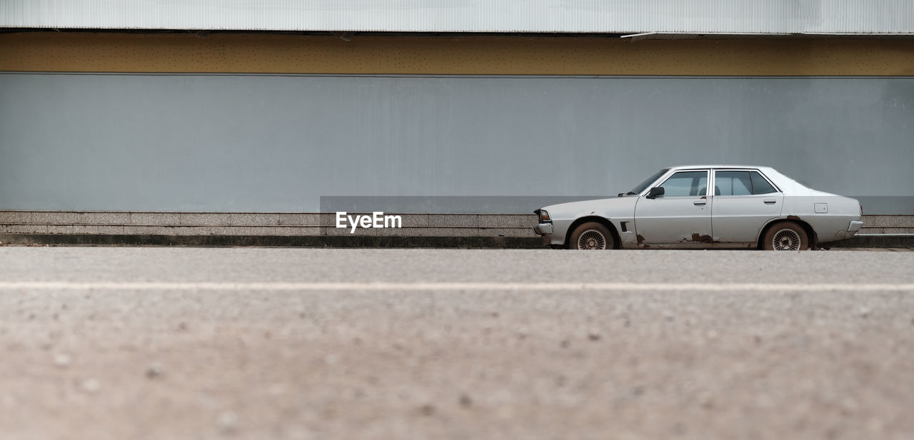 An old, broken car parked next to an advertising space and a foreground, blurry road