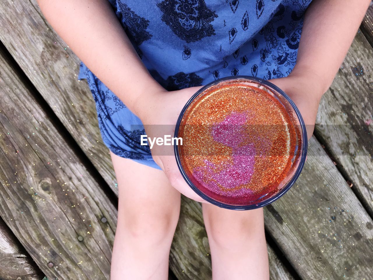 Midsection of woman holding glitter while sitting on wood