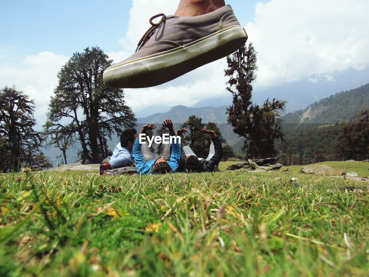 Low section of person over men lying on field against sky