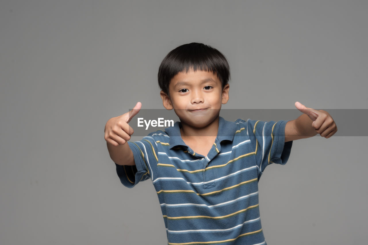 Portrait of boy gesturing thumbs up sign against gray background