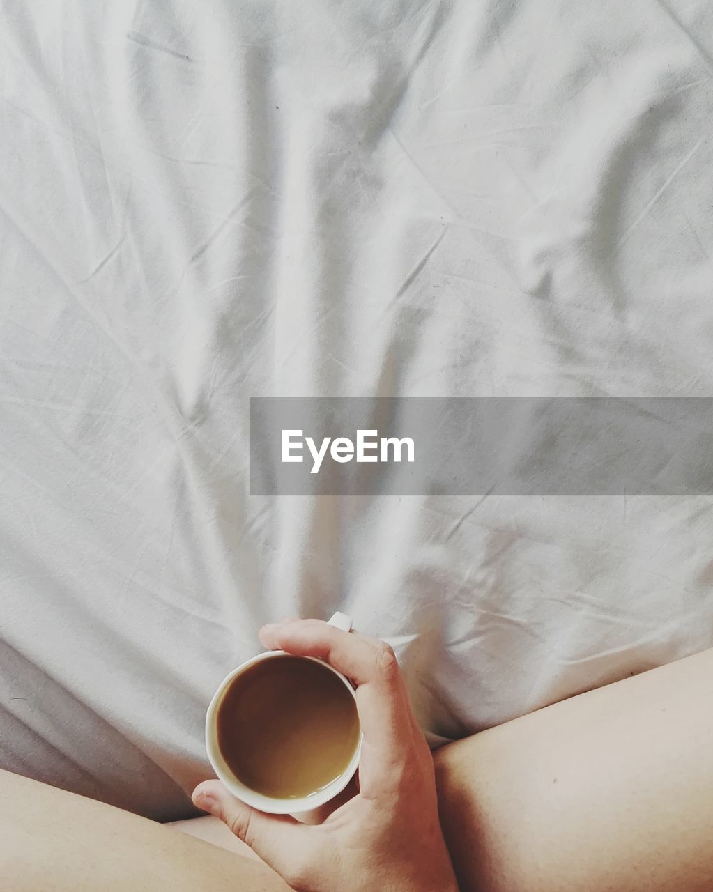 Low section of woman holding coffee cup on bed