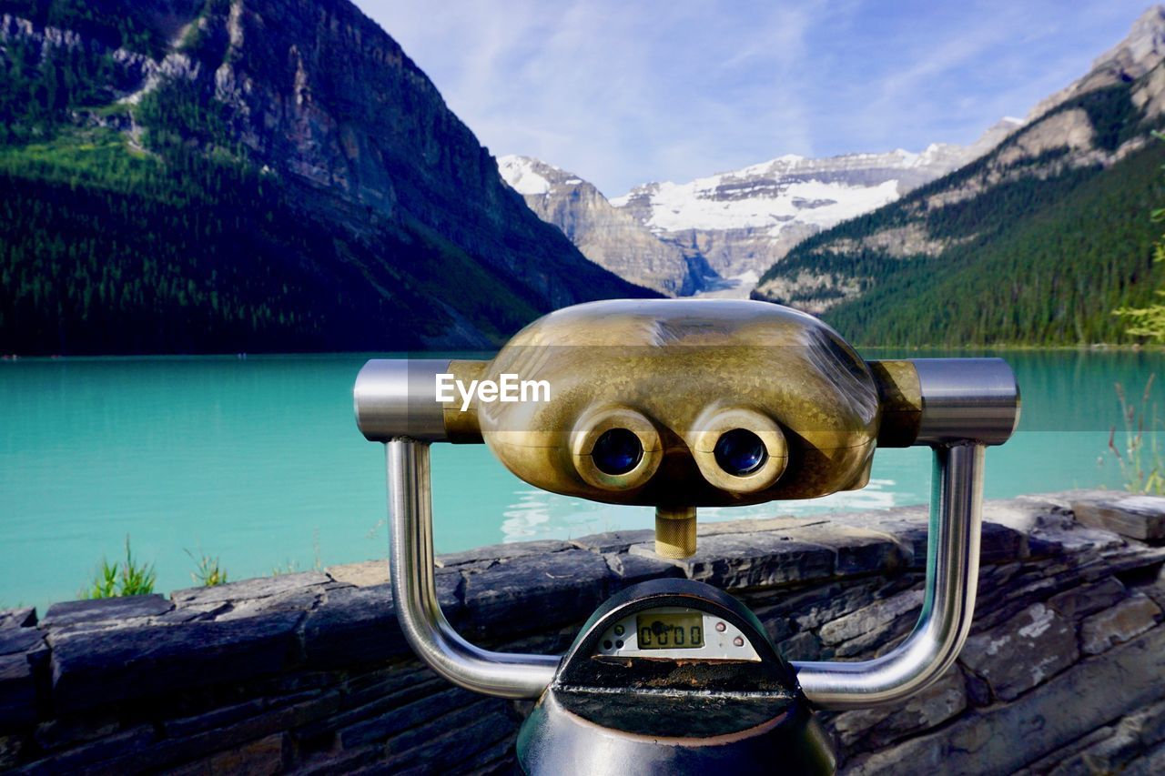 Close-up of coin-operated binoculars by lake against mountains