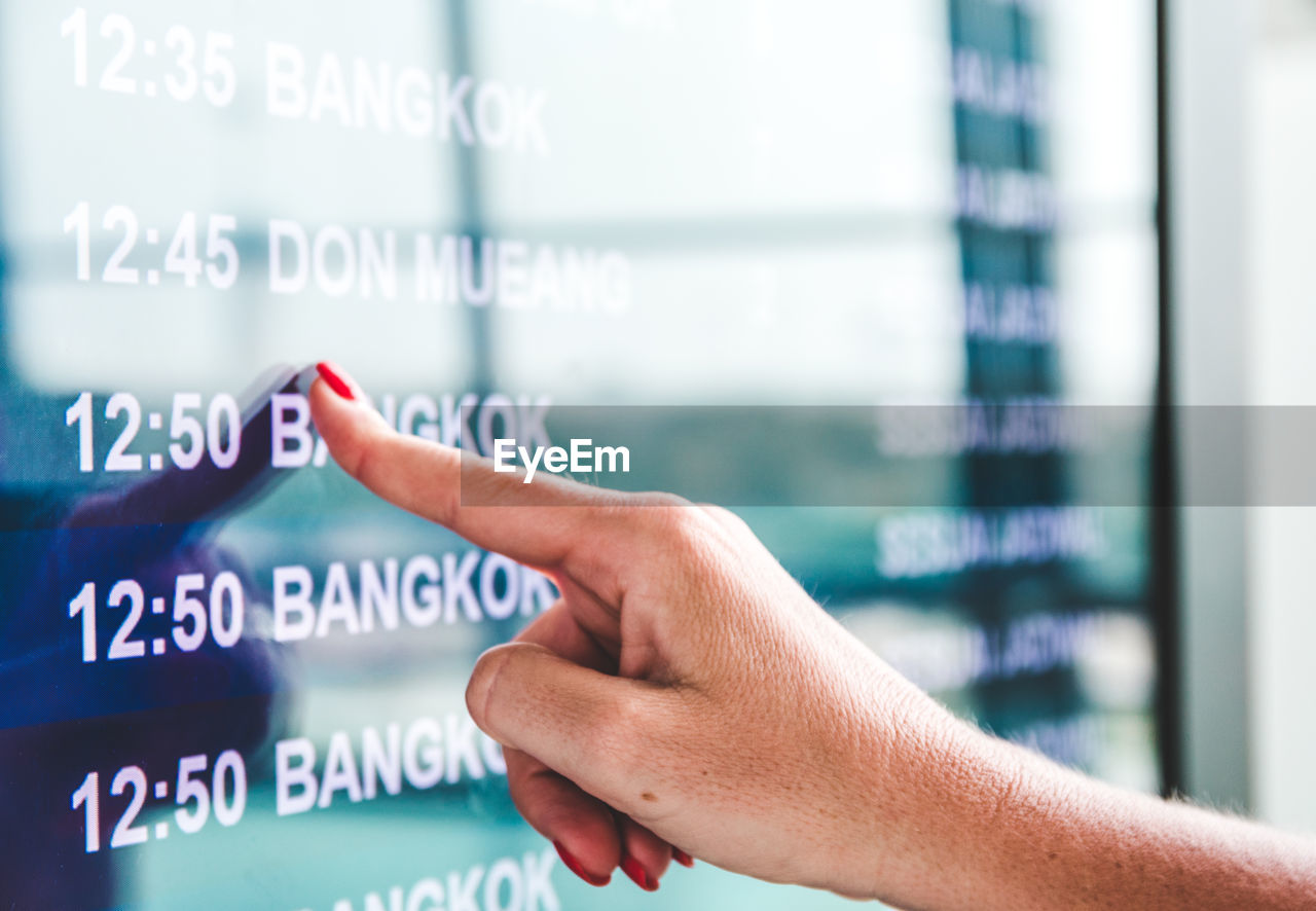 Cropped hand checking arrival departure board at airport