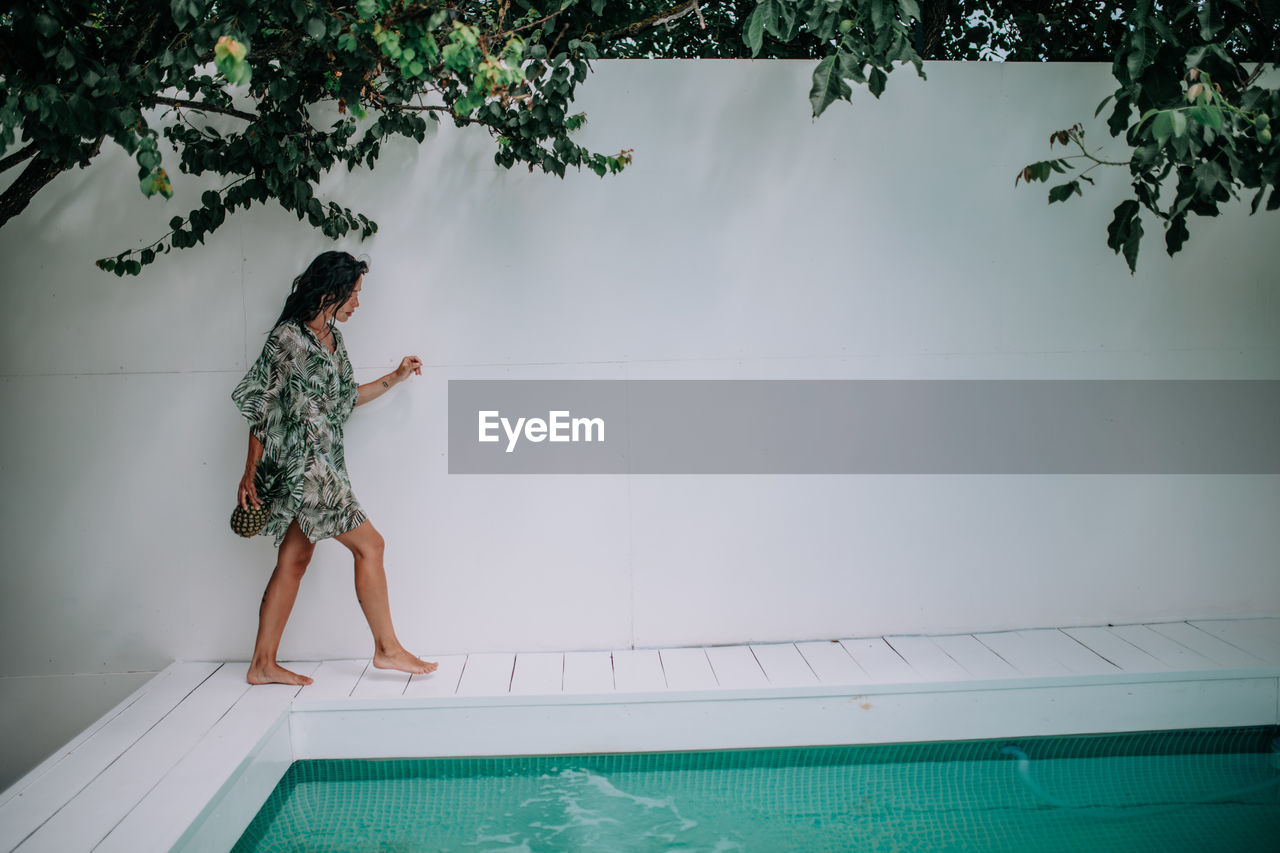 Woman standing by swimming pool against trees