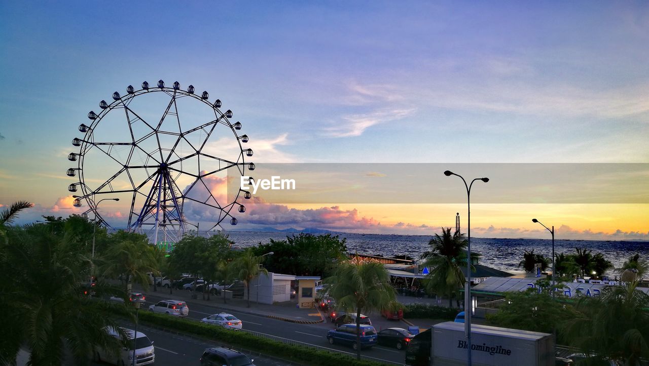 FERRIS WHEEL BY STREET AGAINST SKY DURING SUNSET