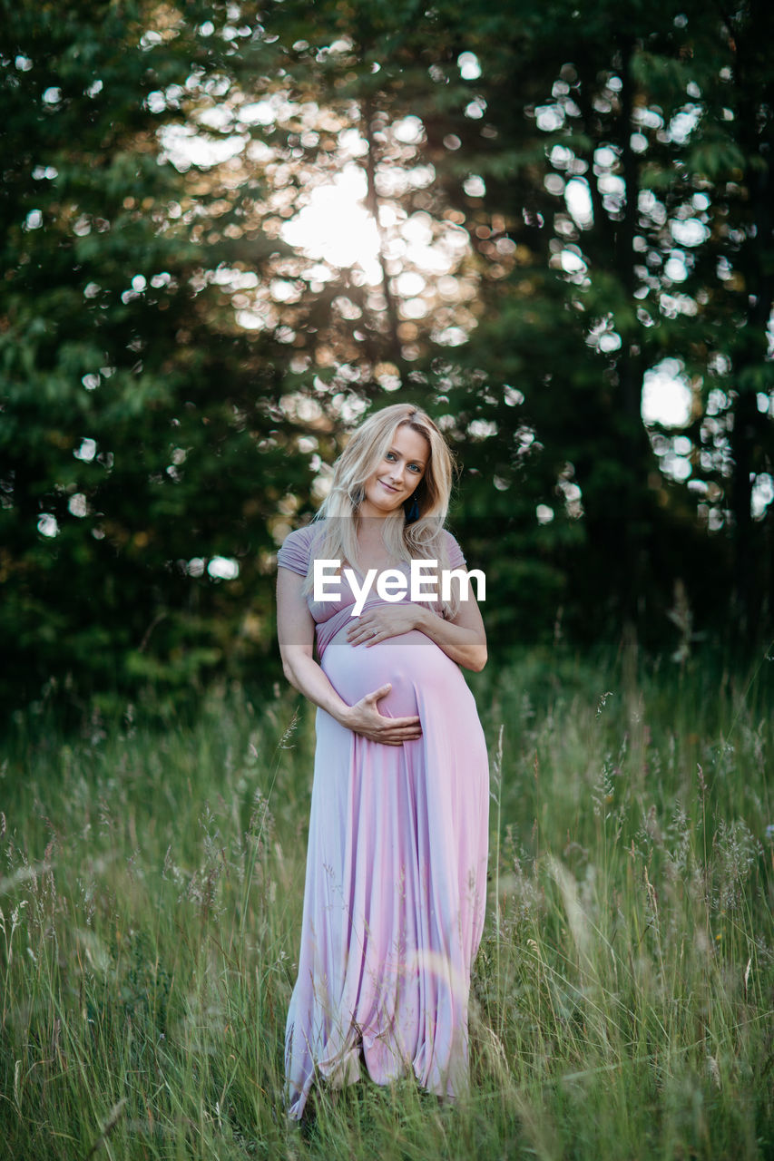 Happy pregnant woman standing on field