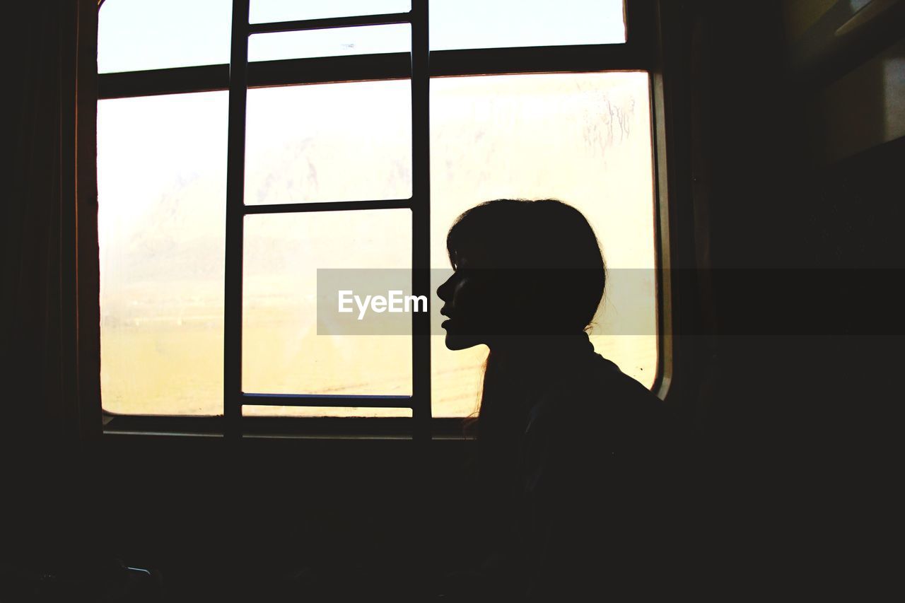 Side view of silhouette young woman sitting by window in train during sunset