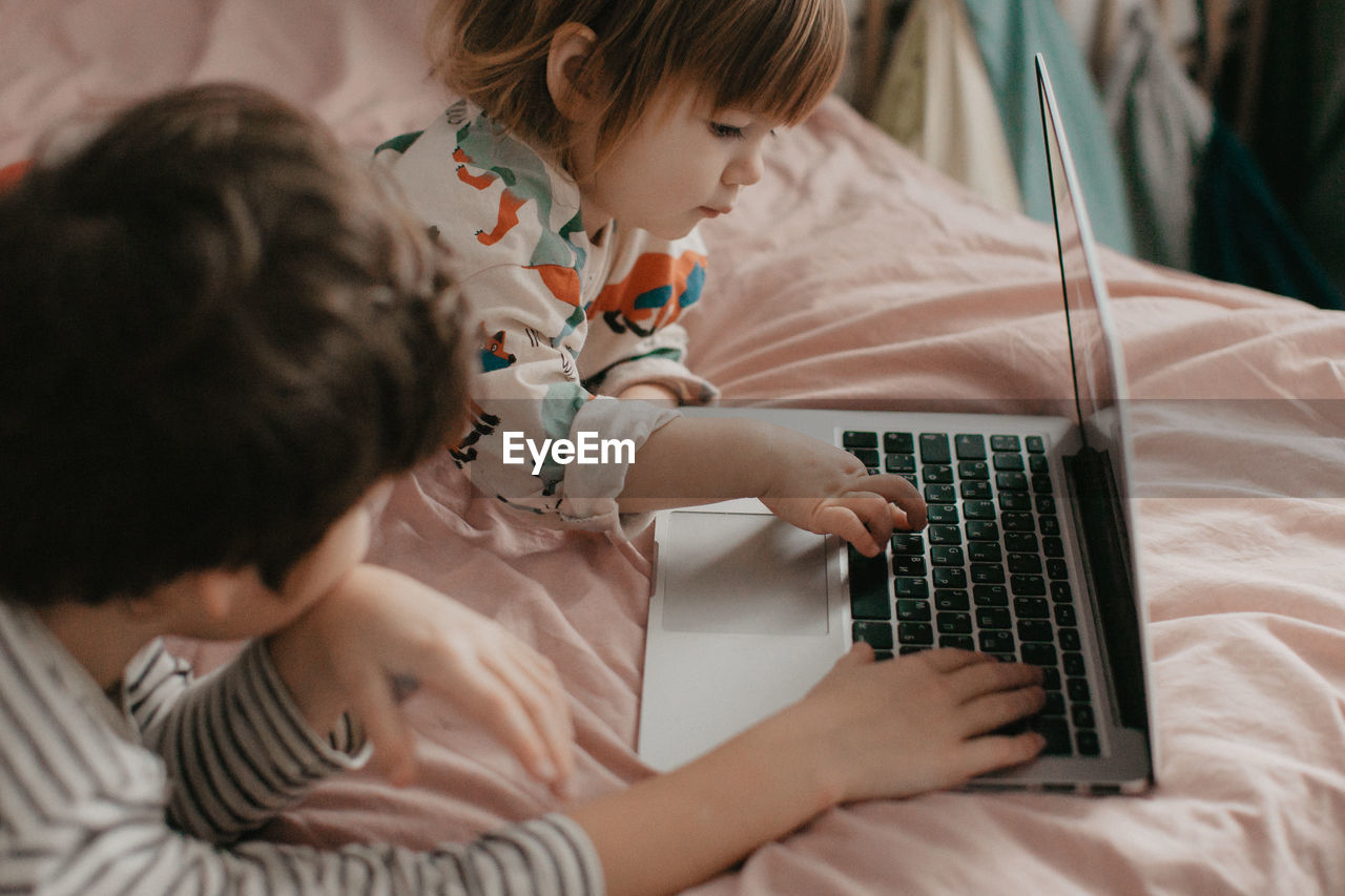 Little brother and sister lie in the bedroom on the bed and look at the laptop. high quality photo