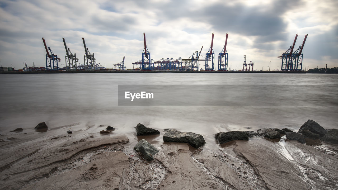 Cranes at commercial dock against sky