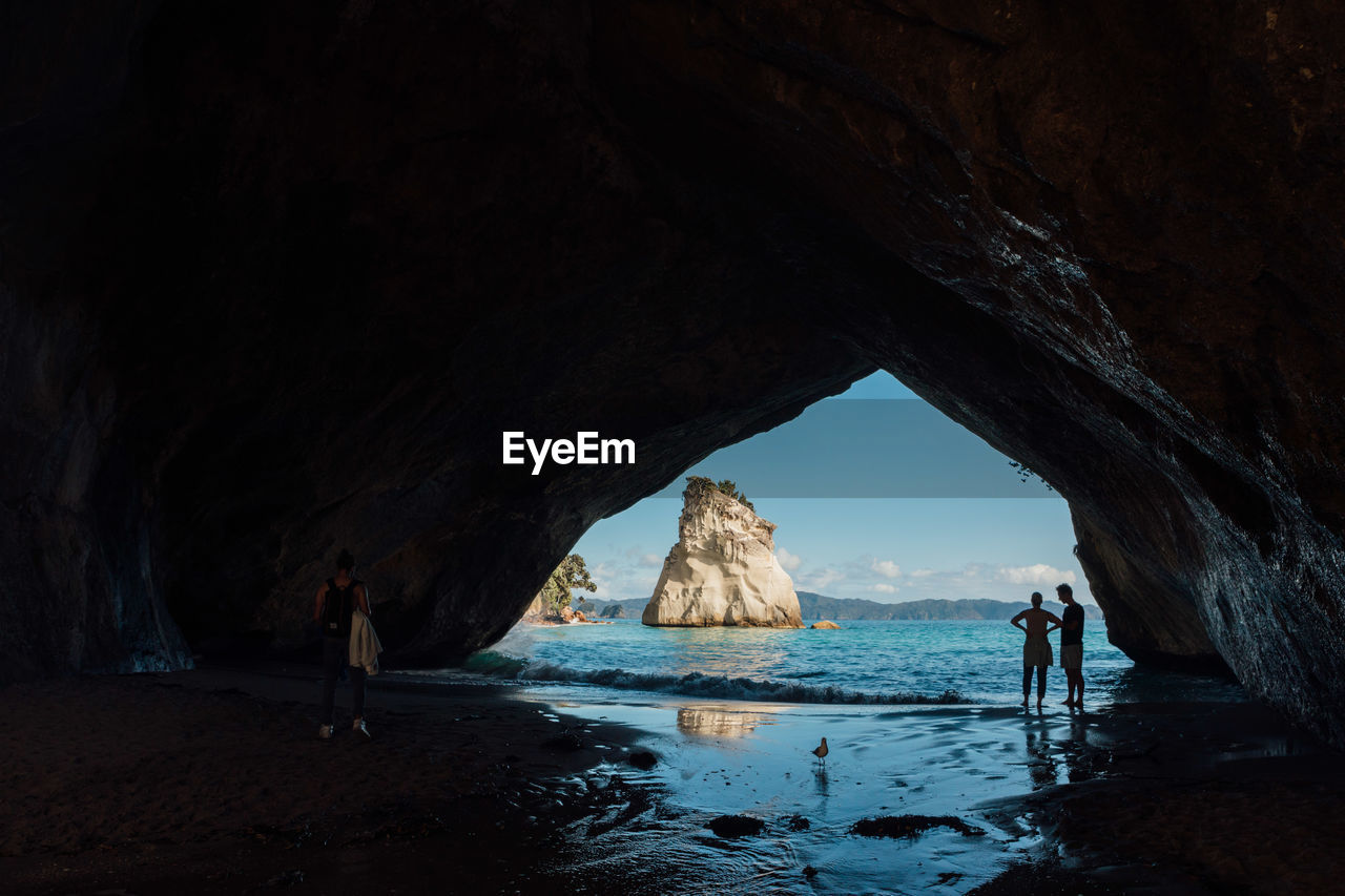 Silhouette couple standing on shore seen through cave