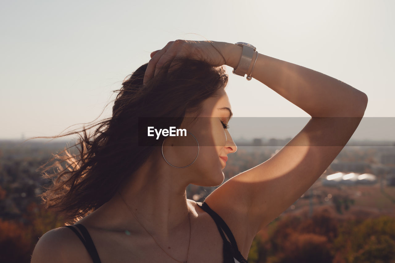 Beautiful woman with hand in hair standing against clear sky during sunny day