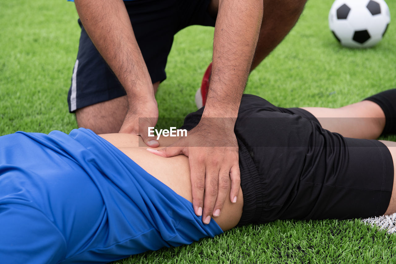 Midsection of man massaging friend back on soccer field