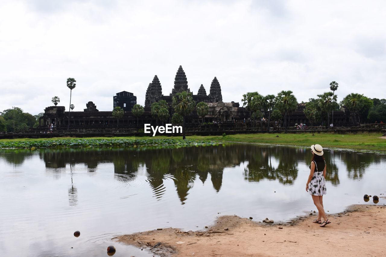 Rear view of woman standing by lake at angkor wat against sky