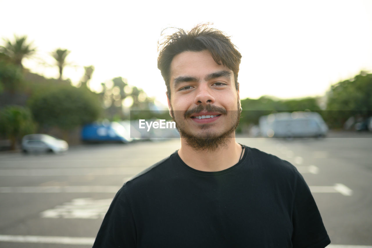 portrait of young man standing on street against sky