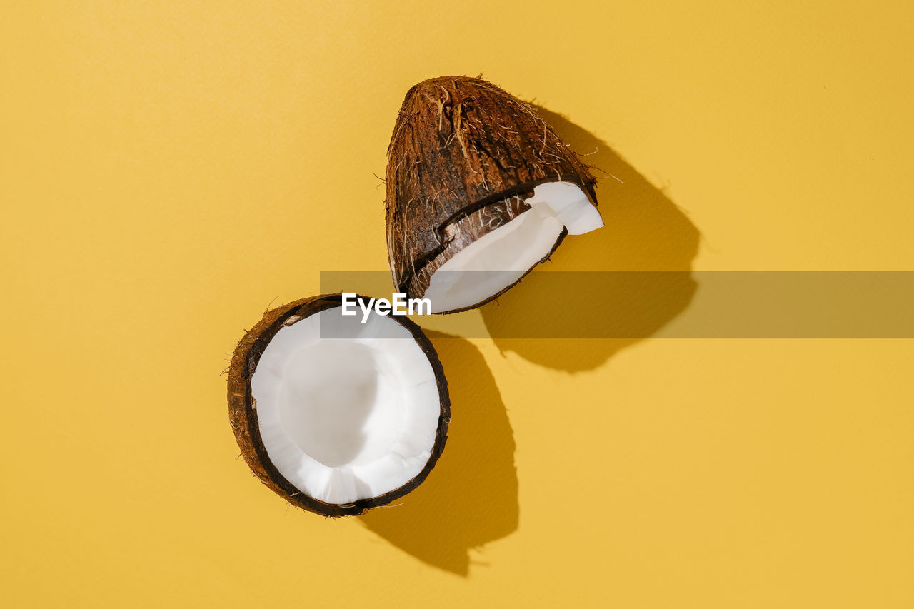Two halves of coconut on a bright yellow background.