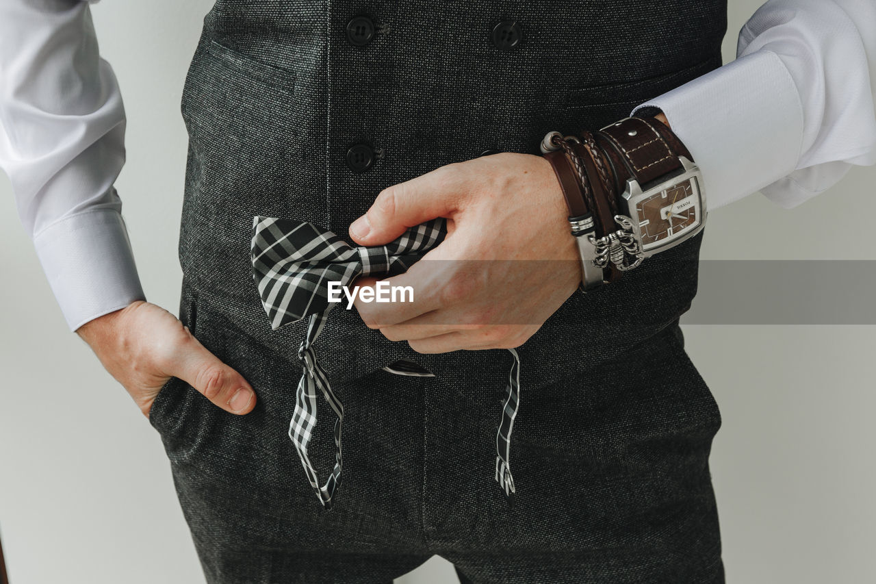 Midsection of man holding bow tie against white background