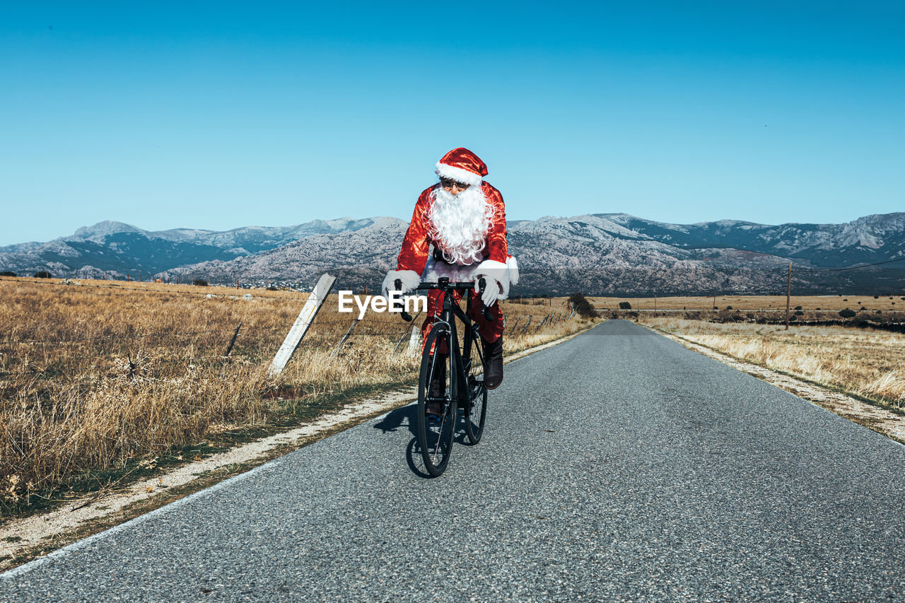 Santa claus in red costume riding modern bike along empty road in highlands on sunny day