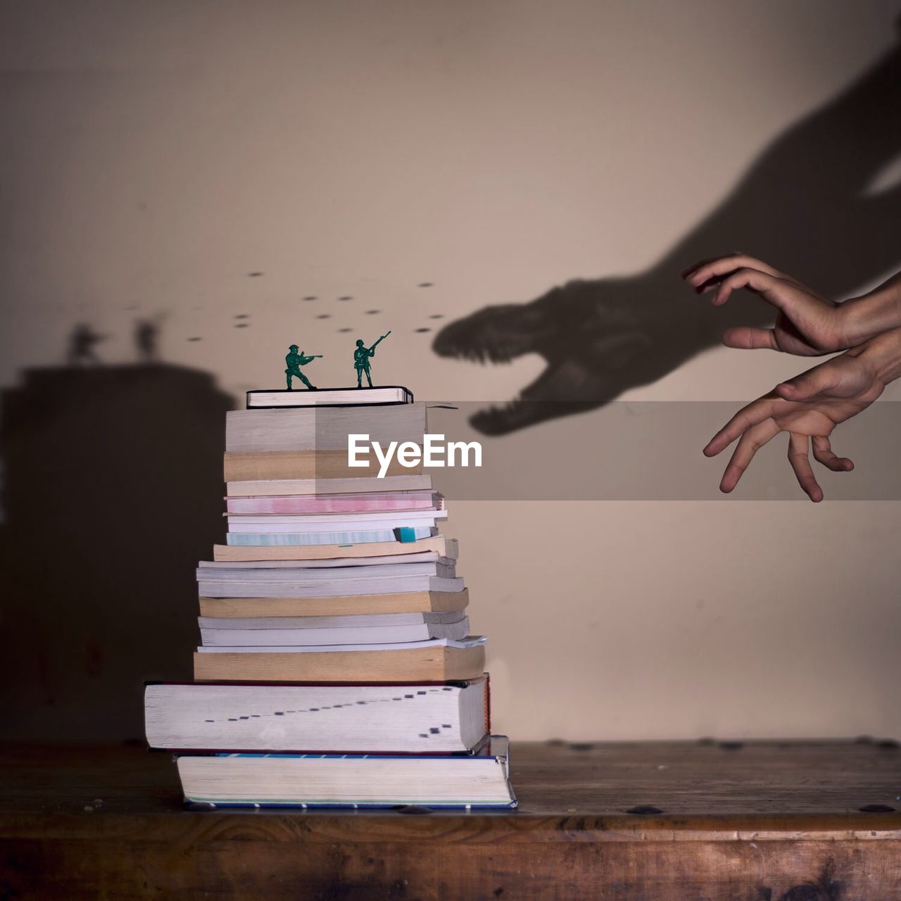 Cropped image of hands making dinosaur shadow attacking on soldier figurines on books