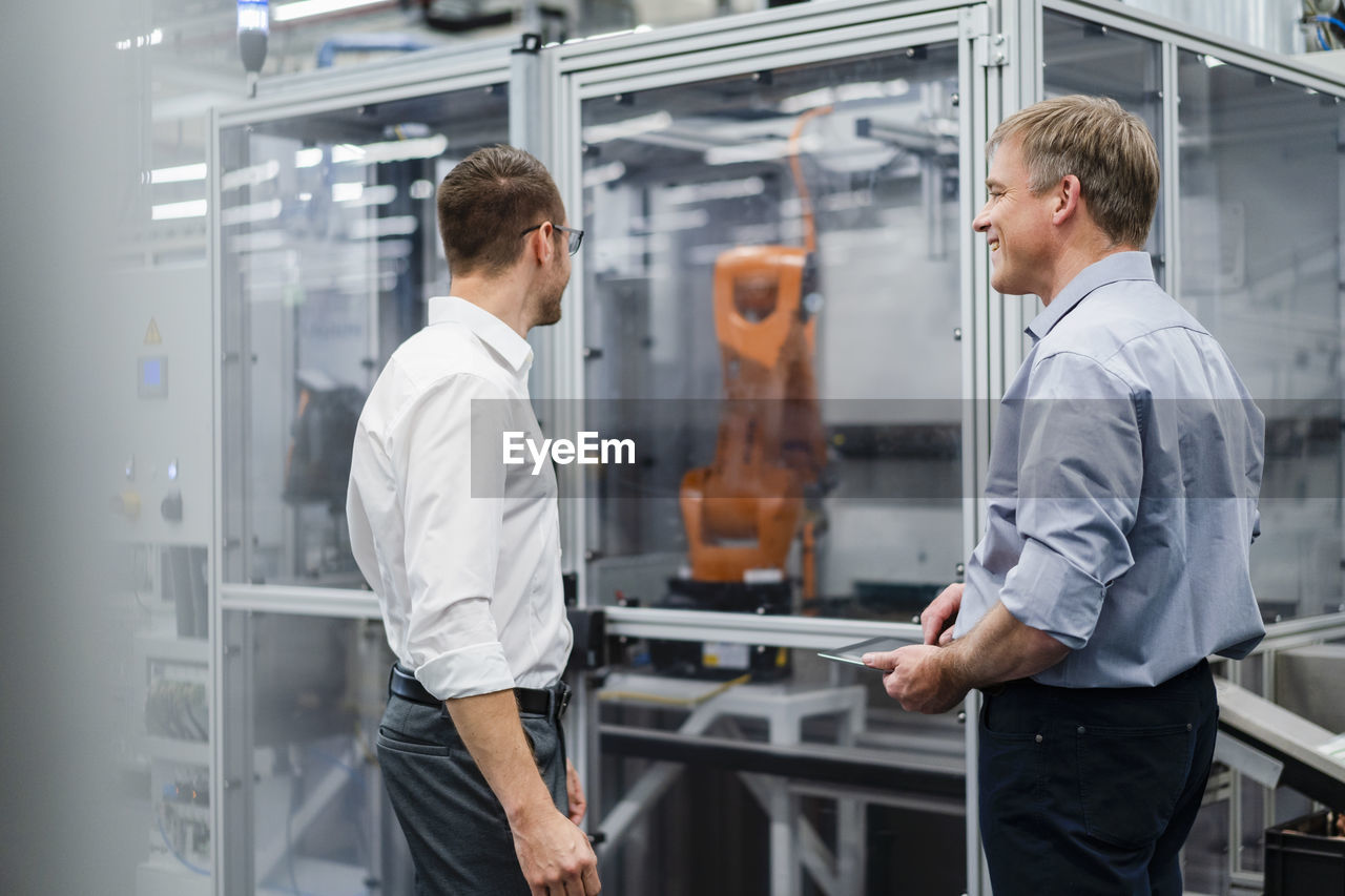 Two businessmen having a meeting at industrial robot in a factory