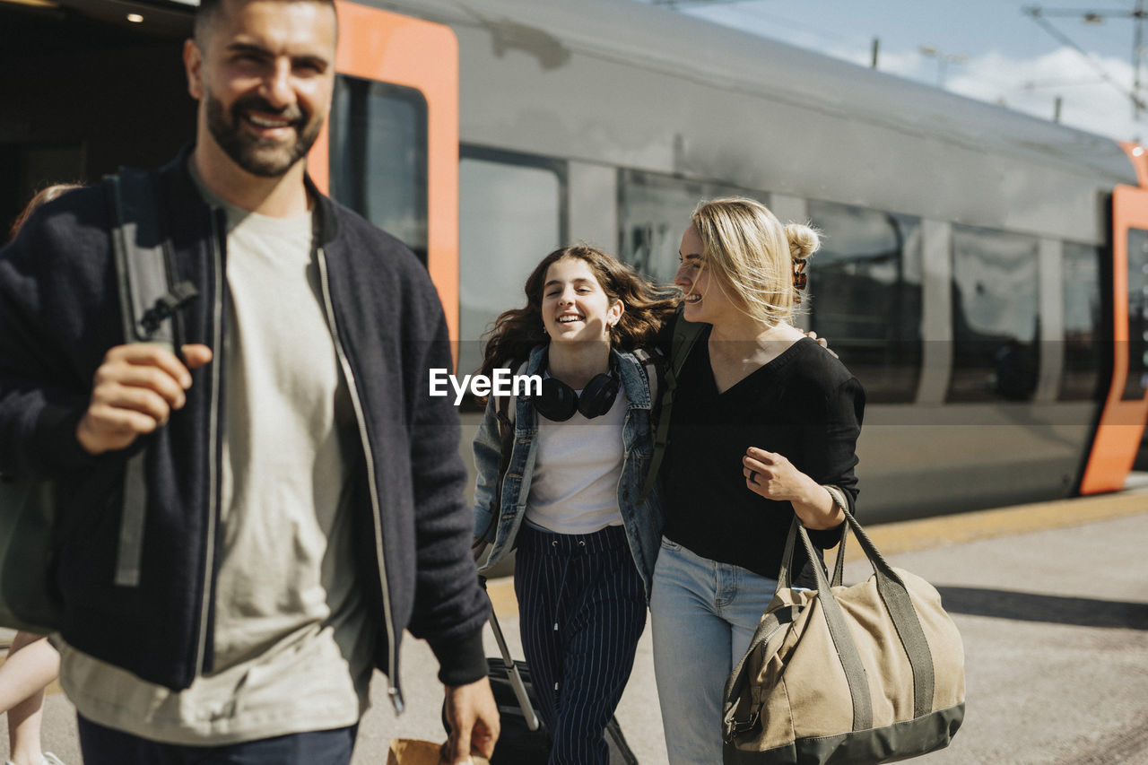 Happy family disembarking from train at station during sunny day